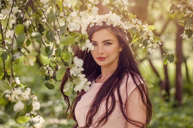 Jonge vrouw met voorjaarsbloemen buiten Mooie brunette modemodel meisje met lang gezond haar en make-up op groene bladeren en witte bloemen achtergrond buiten