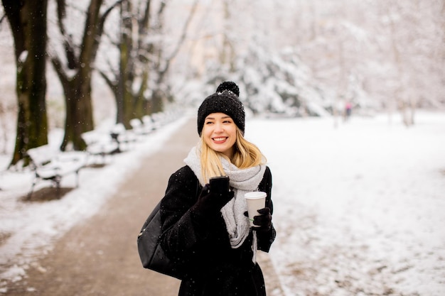 Jonge vrouw met warme kleren in koude wintersneeuw die koffie drinkt om te gaan