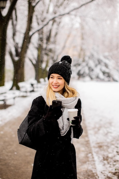 Jonge vrouw met warme kleren in koude wintersneeuw die koffie drinkt om te gaan