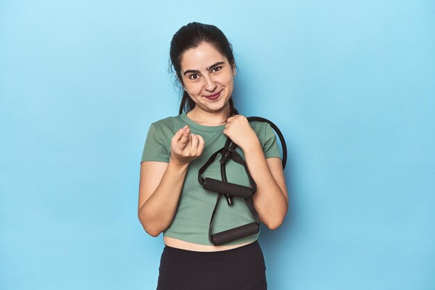 Jonge vrouw met weerstandsbanden op blauw wijst met de vinger naar je alsof ze uitnodigt om dichterbij te komen