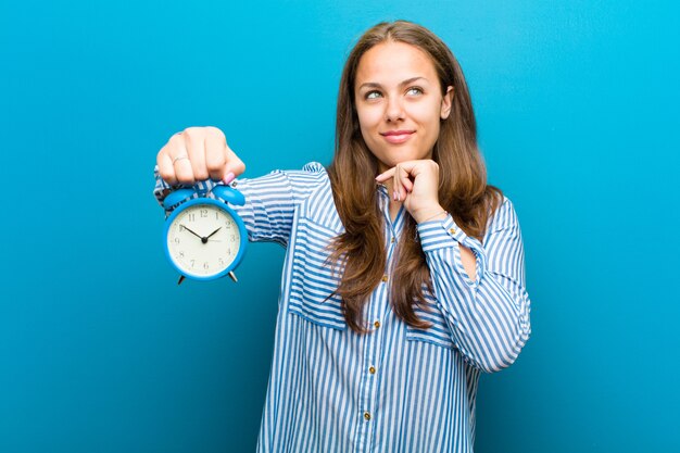 Jonge vrouw met wekker op blauw