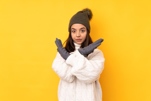 Jonge vrouw met wintermuts over geïsoleerde gele achtergrond die GEEN gebaar maakt