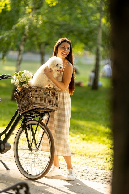 Jonge vrouw met witte bichon frise hond in de mand van elektrische fiets