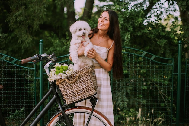 Jonge vrouw met witte bichon frise hond in de mand van elektrische fiets