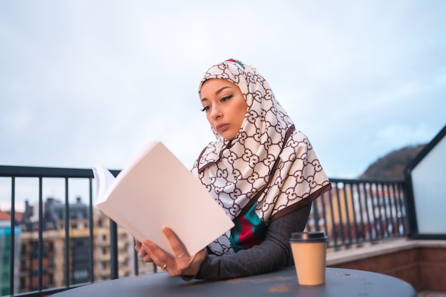 jonge vrouw met witte sluier achter de computer op het terras van een coffeeshop, een mooi boek lezen