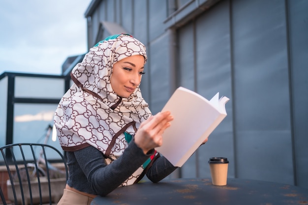 jonge vrouw met witte sluier achter de computer op het terras van een coffeeshop, met veel plezier bij het lezen van een mooi boek