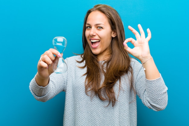 Jonge vrouw met zandloper tegen blauw