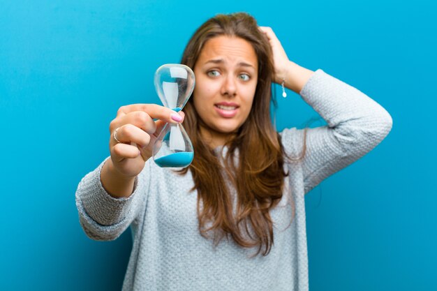 Jonge vrouw met zandloper tegen blauw