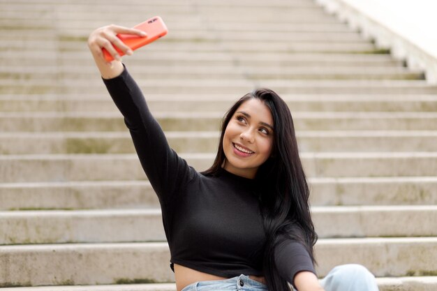 Jonge vrouw met zwart haar glimlachend die selfies neemt met haar telefoon