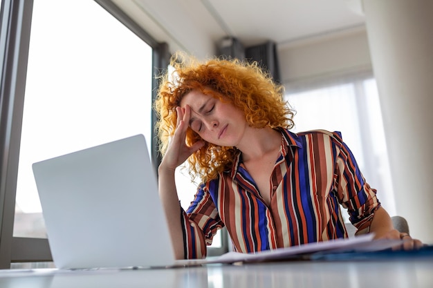 Jonge vrouw moe uitgeput van hard studeren Verveeld en gefrustreerd Hoofd rustend op de hand Heldere ruimte grote ramen Thuis concept Stress concept