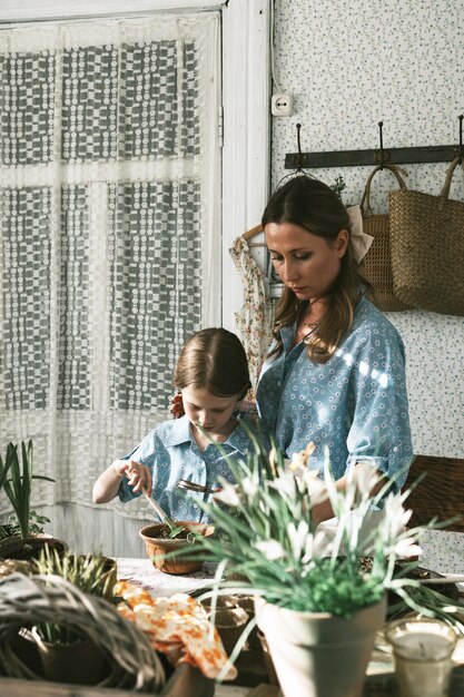 Jonge vrouw moeder en haar kleine dochter in familie look jurken zijn het planten van bloemen op het lente terras in het huis tuin zaailingen groeien landhuis veranda moederschap