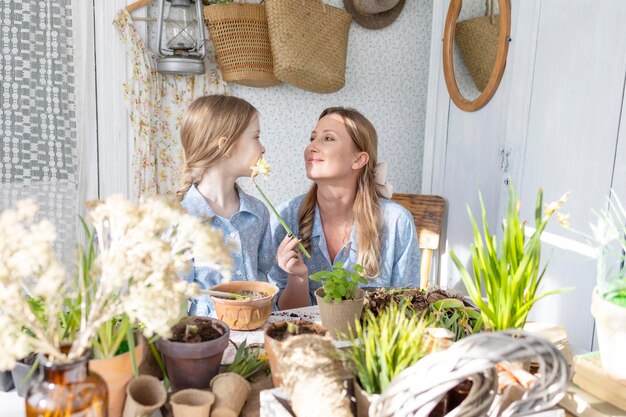 Jonge vrouw moeder en haar kleine dochter in familie look jurken zijn het planten van bloemen op het lente terras in het huis tuin zaailingen groeien landhuis veranda moederschap