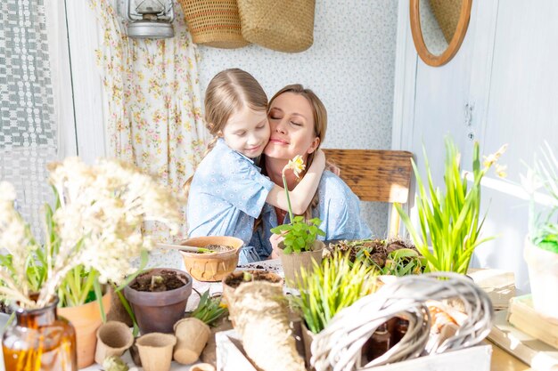 Foto jonge vrouw moeder en haar kleine dochter in familie look jurken zijn het planten van bloemen op het lente terras in het huis tuin zaailingen groeien landhuis veranda moederschap