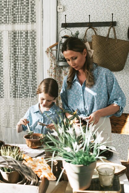 Foto jonge vrouw moeder en haar kleine dochter in familie look jurken zijn het planten van bloemen op het lente terras in het huis tuin zaailingen groeien landhuis veranda moederschap