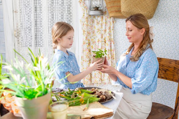 Foto jonge vrouw moeder en haar kleine dochter in familie look jurken zijn het planten van bloemen op het lente terras in het huis tuin zaailingen groeien landhuis veranda moederschap