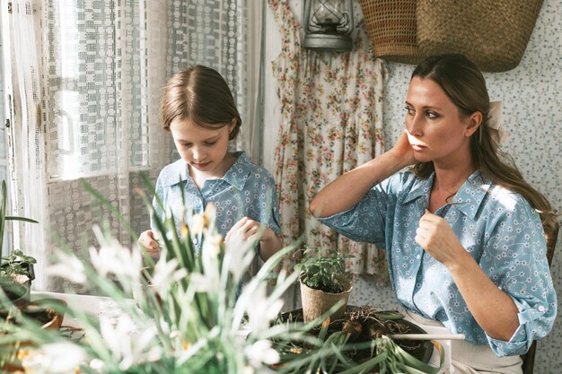 Jonge vrouw moeder en haar kleine dochter in familie look jurken zijn het planten van bloemen op het lente terras in het huis tuin zaailingen groeien landhuis veranda moederschap