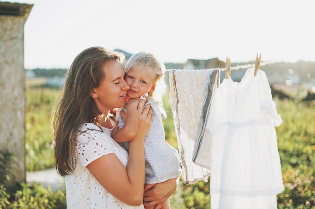 Jonge vrouw moeder met babymeisje op handen knuffelen in achtertuin van huisje in het zonsonderganglicht