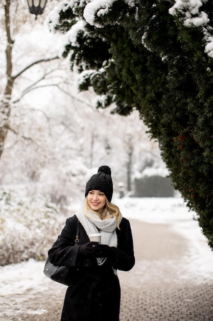 Jonge vrouw n warme kleren genieten in de sneeuw met afhaalkoffiekopje