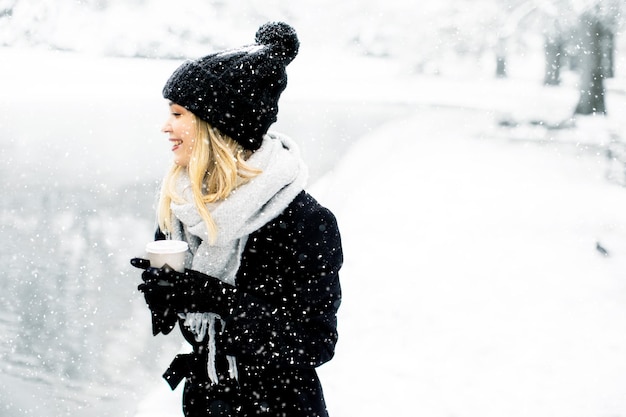 Jonge vrouw n warme kleren genieten in de sneeuw met afhaalkoffiekopje