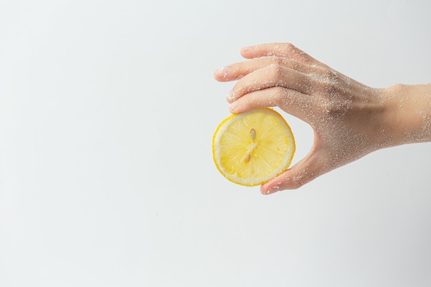 Jonge vrouw natuurlijke citroen scrub toe te passen op handen tegen wit oppervlak