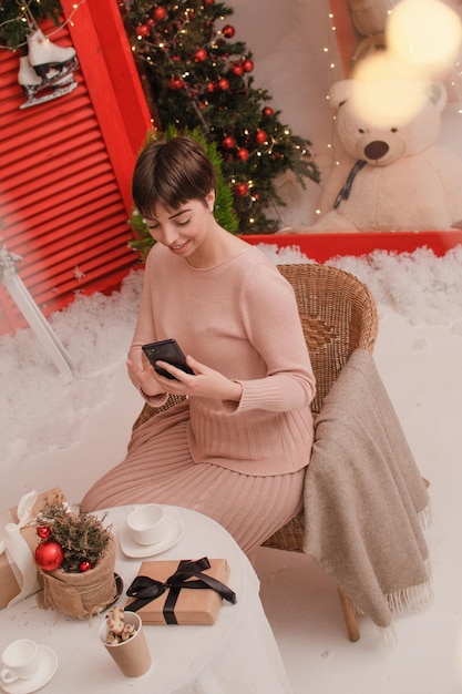 Jonge vrouw neemt fotogeschenkdoos op feestelijke tafel met sparsamenstelling, kersttijd