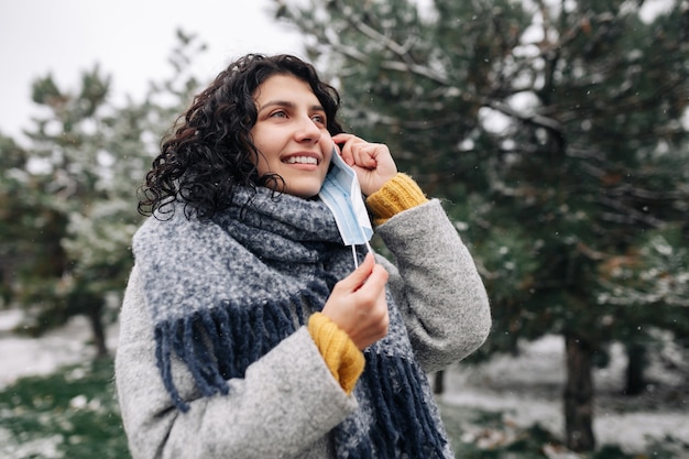 Jonge vrouw neemt het medisch steriele masker over in een winters sneeuwpark op een koude ijzige dag.