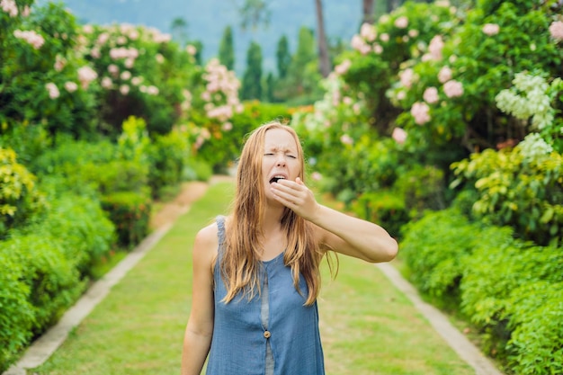 Jonge vrouw niest in het park tegen de achtergrond van een bloeiende boomallergie voor pollenconcept