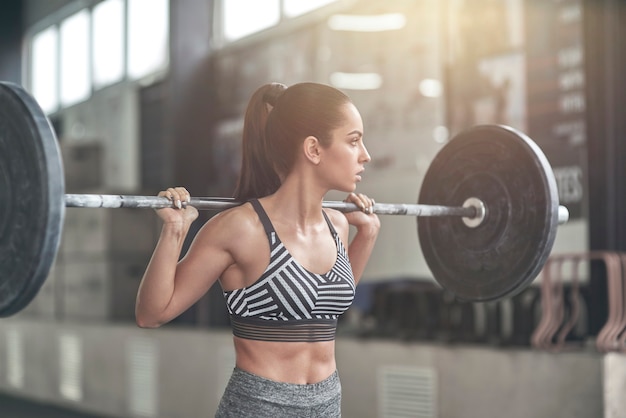 Jonge vrouw oefent in de gezonde levensstijl van de sportschool klaar om de bar op te tillen