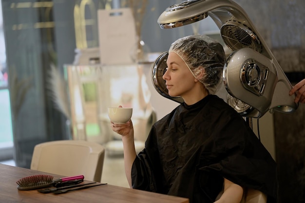 Jonge vrouw onder een droogmachine met kap in kapsalon