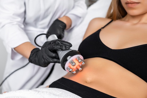 Jonge vrouw ondergaat rf body cavitation lifting om haar buik slanker te maken in de schoonheidssalon