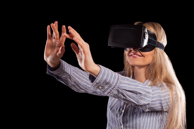 Jonge vrouw ondergedompeld in interactieve virtual reality-videogame die gebaren op zwarte achtergrond doet.