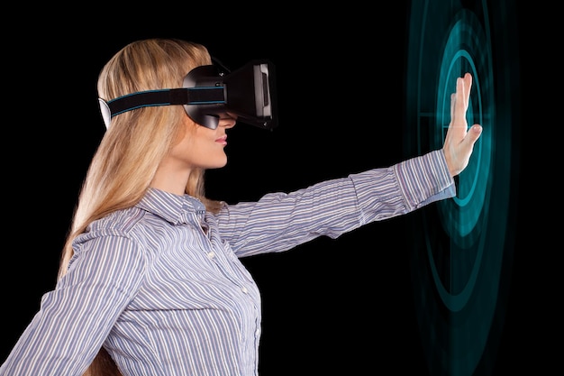 Jonge vrouw ondergedompeld in interactieve virtual reality-videogame die gebaren op zwarte achtergrond doet.