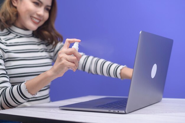 Jonge vrouw ontsmettende alcoholspray met computer, covid-19 beschermingsconcept.