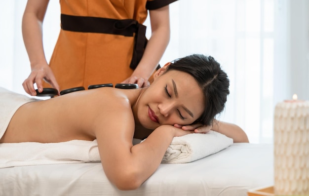 Jonge vrouw ontspannen en genieten in spa salon met hot stone massage Schoonheidsbehandeling therapie