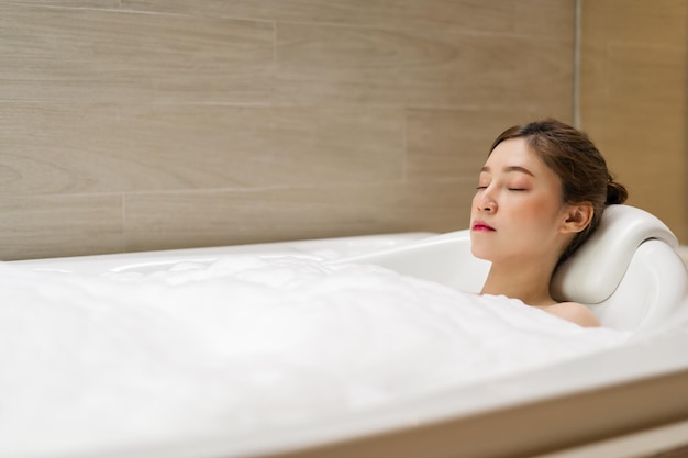 Jonge vrouw ontspannen in bad met gesloten ogen in badkamer