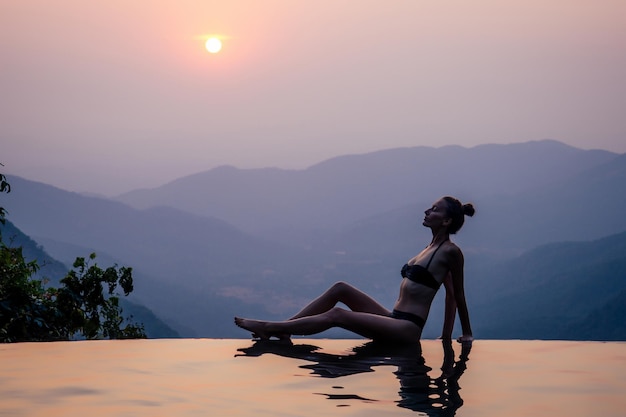 Jonge vrouw ontspannen in het oneindige zwembad kijken naar uitzicht romantische zonsondergang met uitzicht op de heuvels wildernste natuur kuuroord in India Goa Kerala