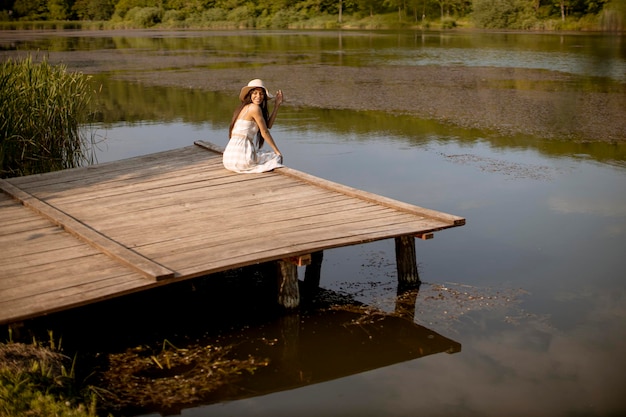 Jonge vrouw ontspannen op de houten pier aan het rustige meer op een hete zomerdag