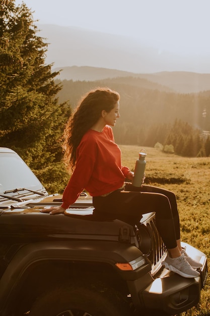Jonge vrouw ontspannen op de motorkap van een terreinvoertuig op het platteland