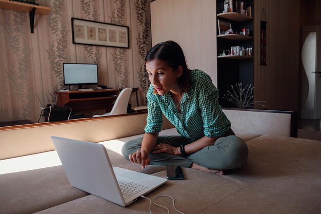 Jonge vrouw op bank die gelukkig aan nieuw project met laptop in huis werkt