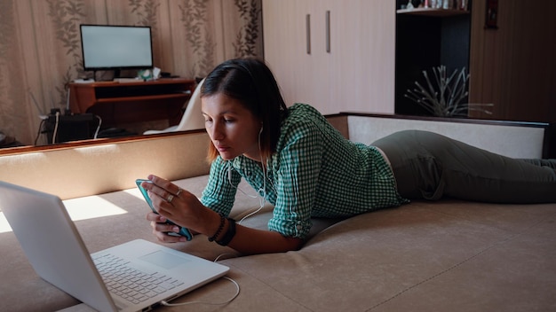 Jonge vrouw op bank die gelukkig aan nieuw project met laptop in huis werkt