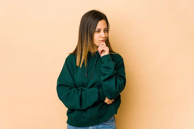 Jonge vrouw op beige muur die en aan een kant denkt bekijkt