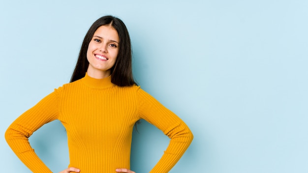 Jonge vrouw op blauwe vertrouwen houden handen op de heupen.