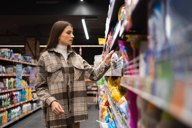 Jonge vrouw op de afdeling huishoudelijke chemie van de supermarkt kiest waspoeder