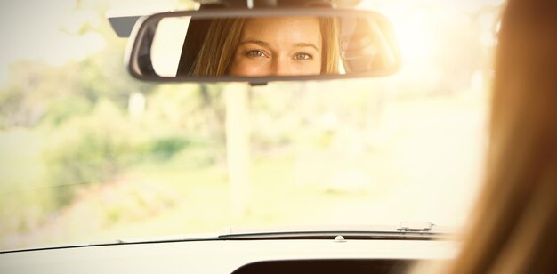 Jonge vrouw op de bestuurdersstoel die in de spiegel van haar auto kijkt