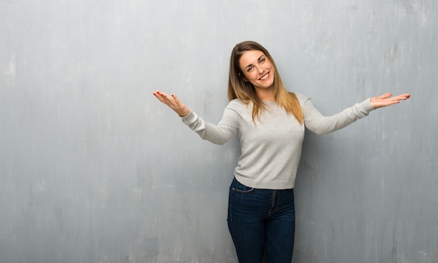 Jonge vrouw op de gestructureerde muur presenteren en uitnodigen om te komen met de hand