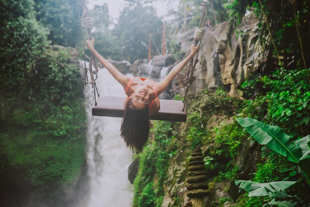 Foto jonge vrouw op de schommel tegen de waterval