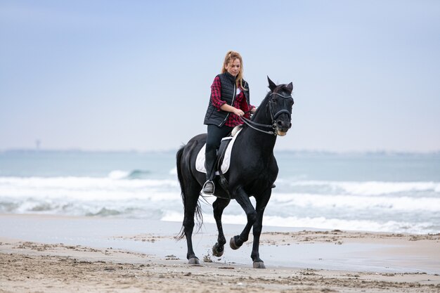 Jonge vrouw op een paard op het strand op een bewolkte dag