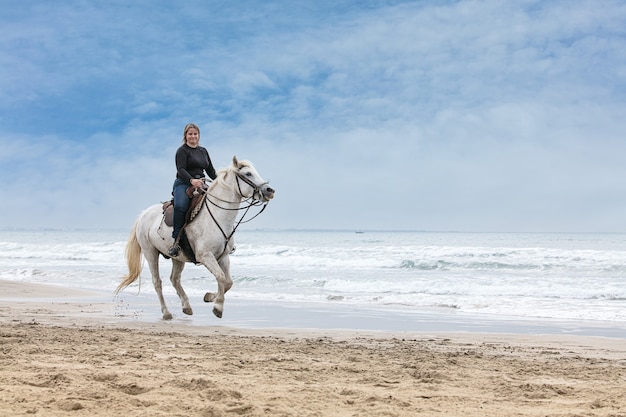 Jonge vrouw op een paard op het strand op een bewolkte dag