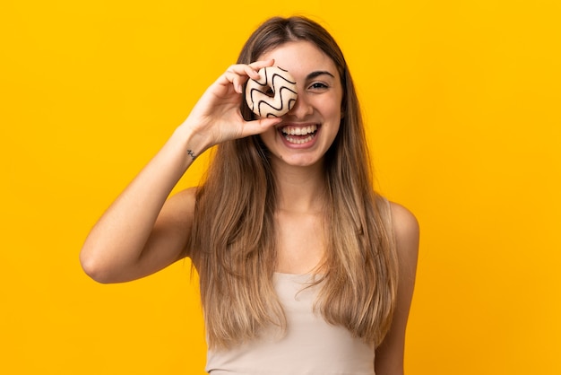 Jonge vrouw op geïsoleerd geel met een doughnut en gelukkig