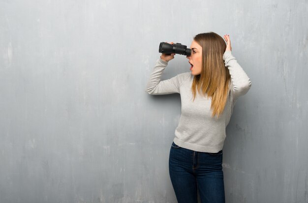 Jonge vrouw op gestructureerde muur en in de verte kijken met een verrekijker